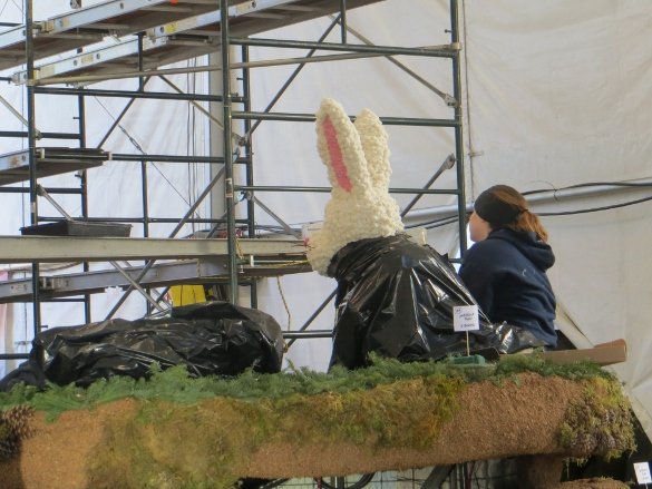 A girl and the bunny both with black jackets watching other decorate from high up on the float.